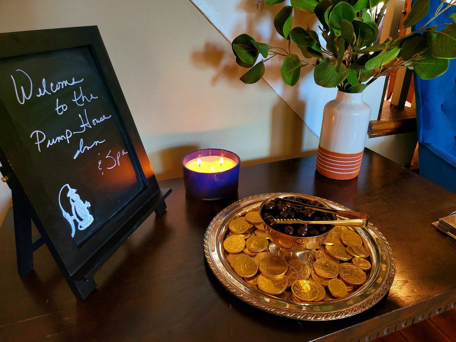 A chalkboard welcome to the Pump House beside a lit candle and a silver tray of chocolate coins.