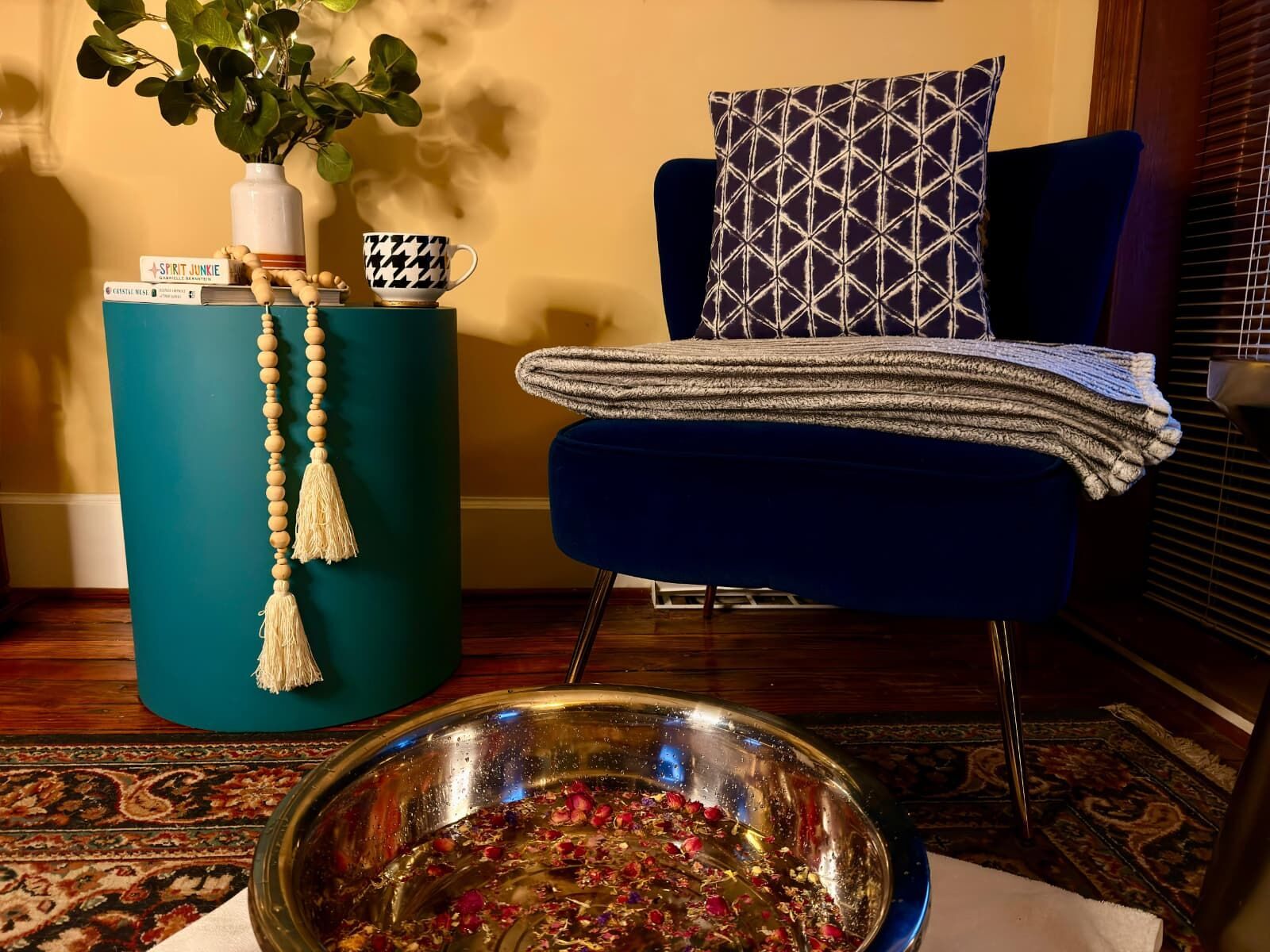 Bare feet resting in a foot spa beside an armchair by a sunlit window, a candle burning on the sill.