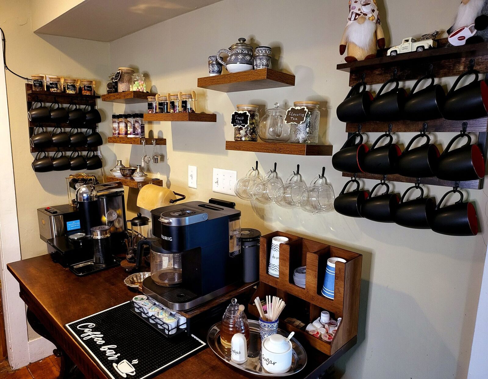 The Pump House coffee and tea station, an antique table with black cups on a wall rack above it.