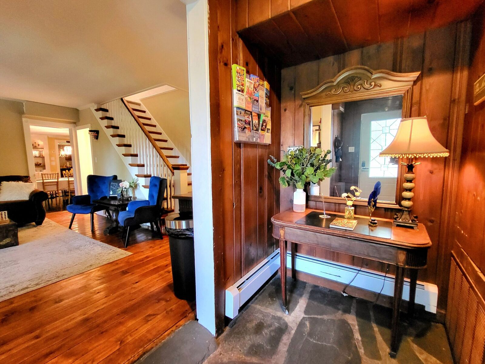 The Pump House front foyer, an old hall table and lamp by the door, the blue velvet chairs by the staircase beyond.